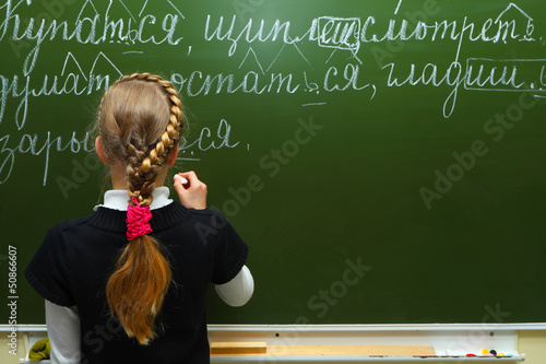 The schoolgirl writes chalk on a blackboard