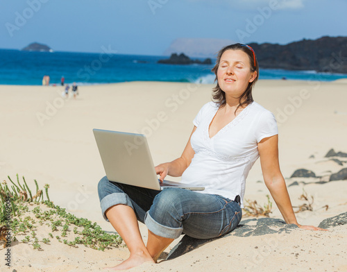 Woman sitting on beach with laptop