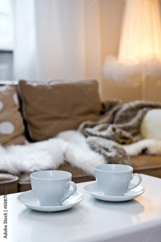 Two coffee cups on the table with sofa with fur cover on it