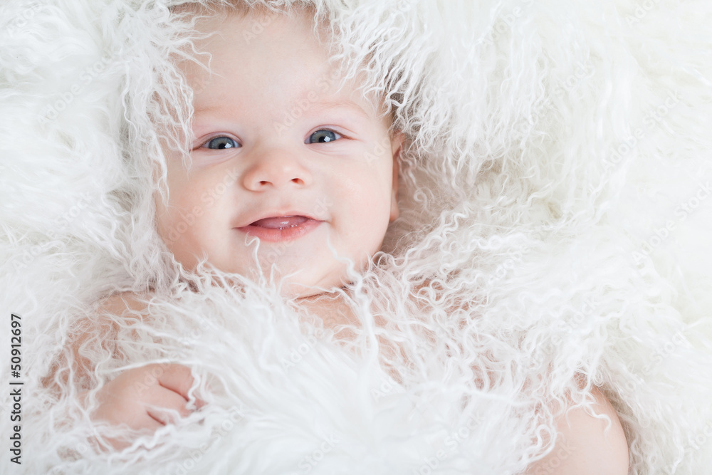 Portrait of a smiling baby wrapped in a white fur.