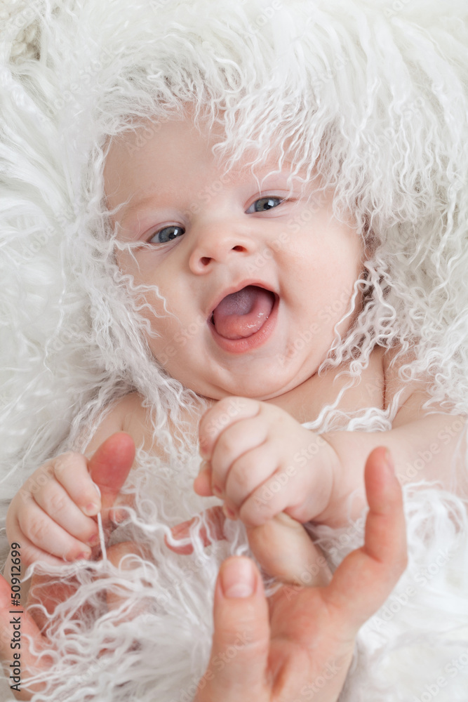 Smiling baby wrapped in a white fur keeps mum's hands. Smiling baby wrapped in a white fur keeps mum's hands.