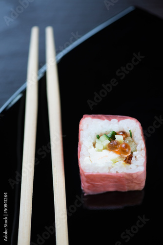 Sushi and chopsticks on a black plate, vertical shot