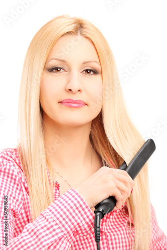 Young blond woman straightening her hair