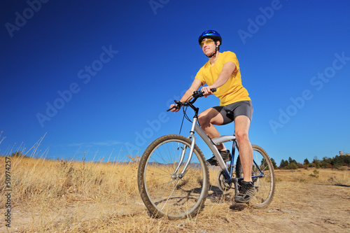 A young male with yellow shirt and helmet riding a bike outdoors