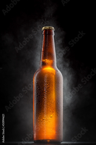 Cold beer bottle with drops, frost and vapour on black
