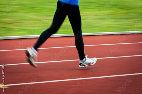 Young woman running at a track and field stadium (motion blurred