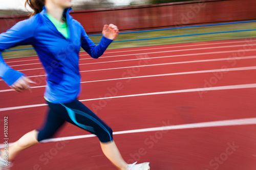 Young woman running at a track and field stadium © lightpoet