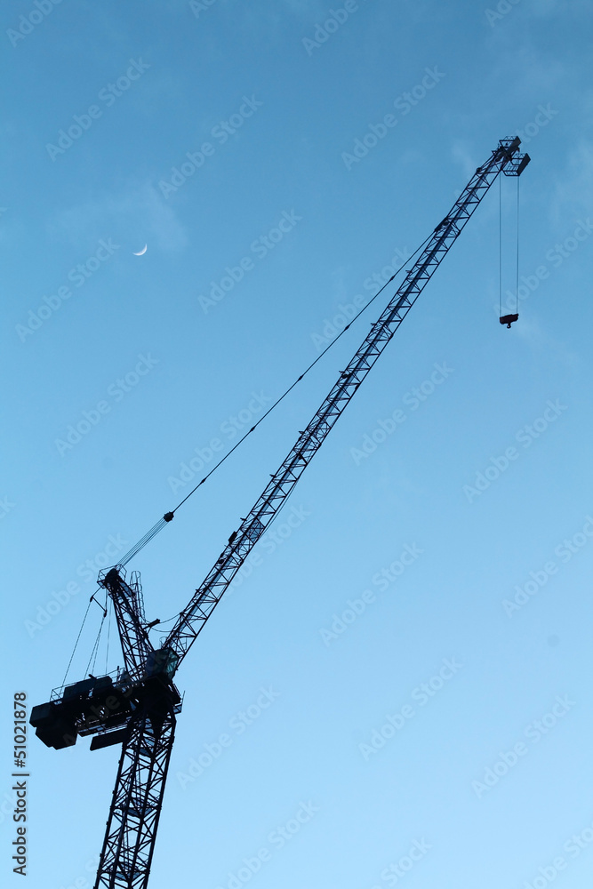 Industrial crane against a blue sky, with the moon behind Industrial crane against a blue sky, with the moon behind