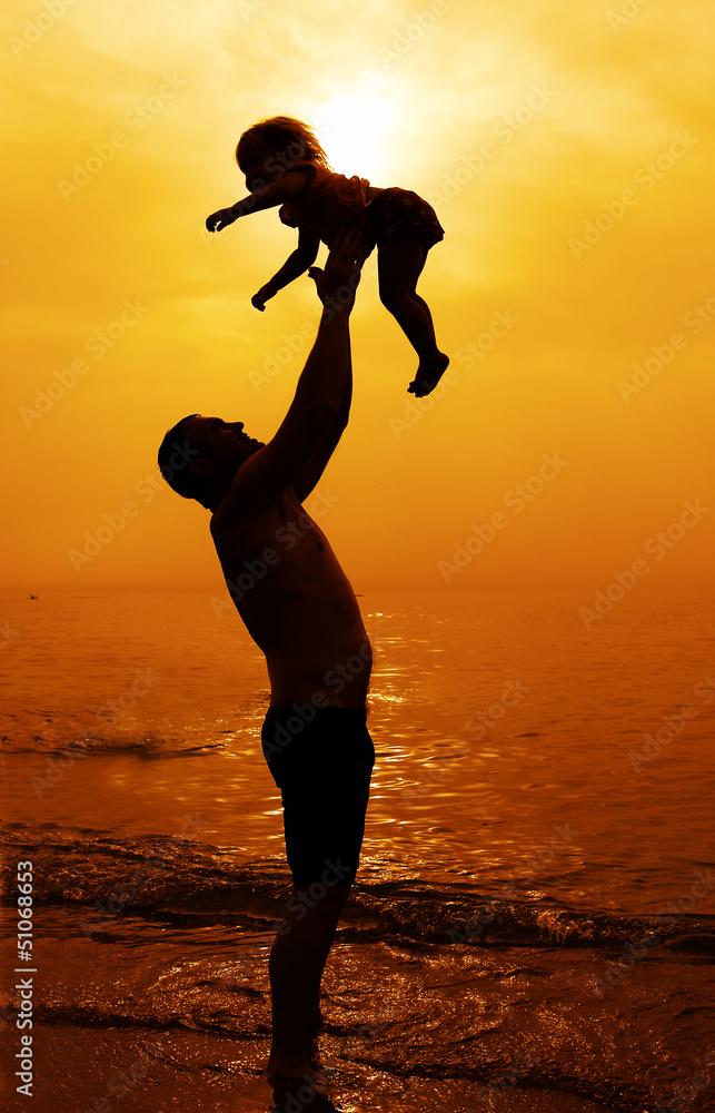 father and daughter playing together on the beach at sunset
