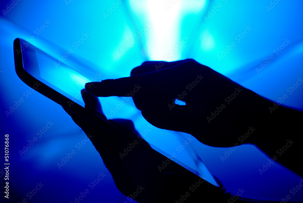 silhouette of hand holding tablet pc over blue