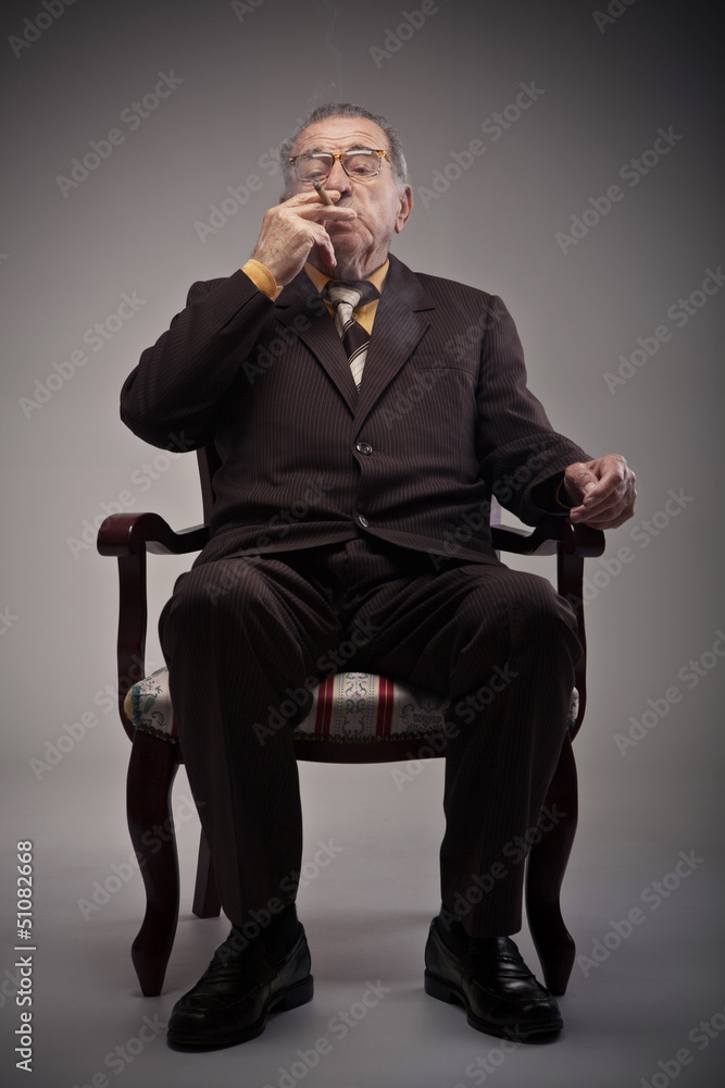 Old man sitting in a chair and smoking a cigarette Old man sitting in a chair and smoking a cigarette