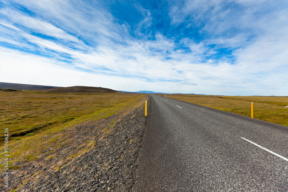 Fototapeta premium Highway through Icelandic landscape under a blue summer sky with