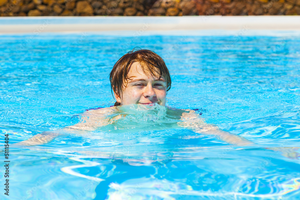 cute handsome teenage boy swims in the pool