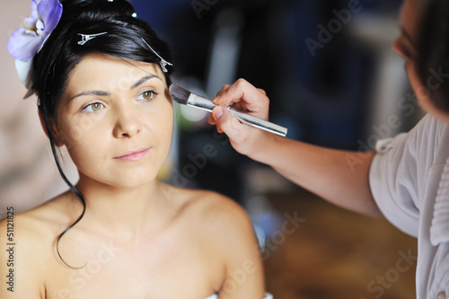 Young beautiful bride applying wedding make-up by make-up artist
