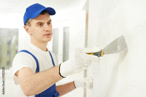 Plasterer with putty knife at wall filling photo