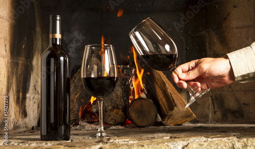Fotografia Copa de vino tinto y botella, con fuego de hogar de fondo.