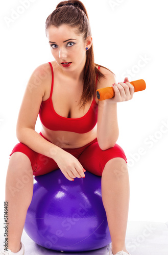 Young pretty woman lifting up dumbbells while sitting on a gym b