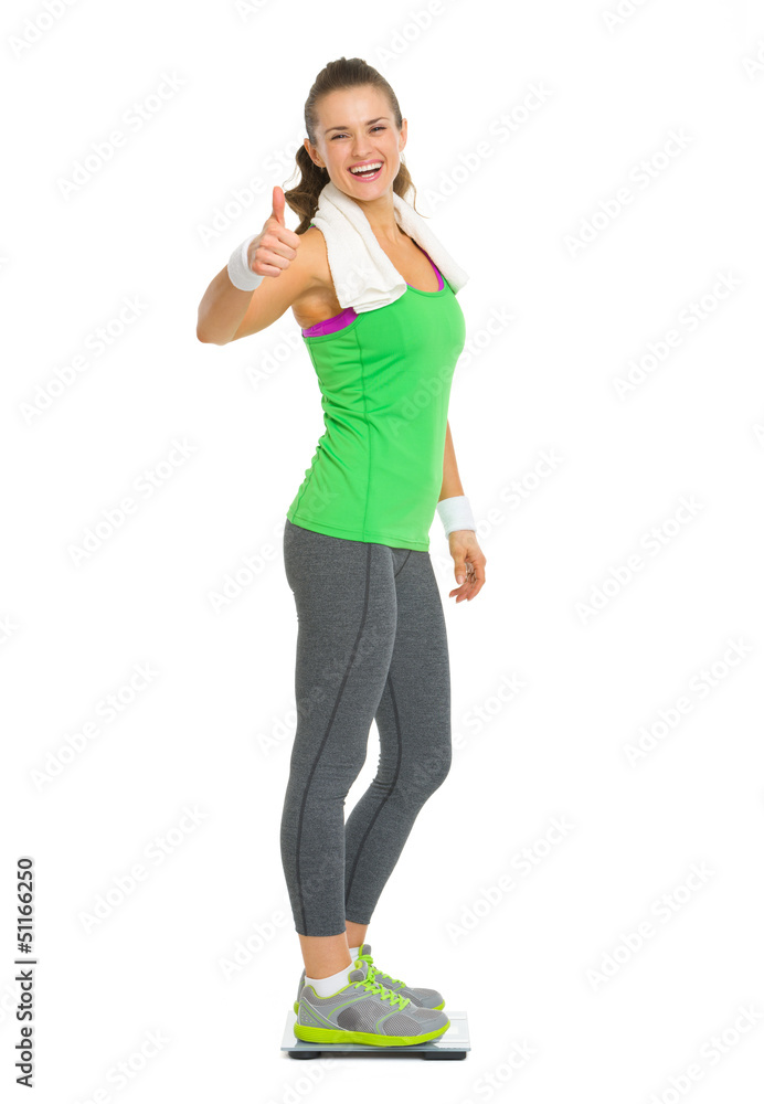 Smiling fitness woman standing on scales and showing thumb up Smiling fitness woman standing on scales and showing thumb up