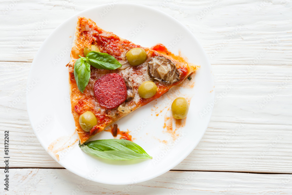 slice of pizza with salami and basil on white plate