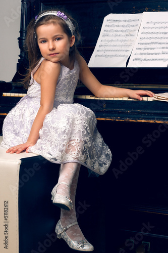 girl in a beautiful dress sits at the piano