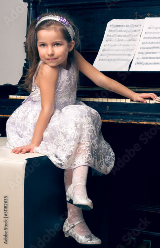 girl in a beautiful dress sits at the piano