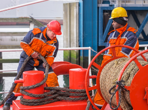 European deck officer working with ropes together with African s photo
