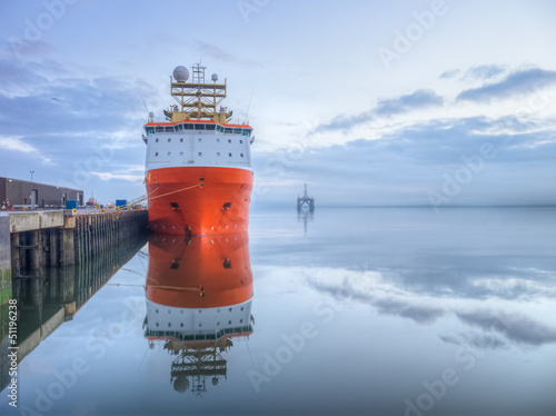 Photography Orange supply vessel in a port with oil rig