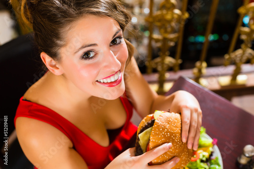 Young woman in fine restaurant  she eats a burger