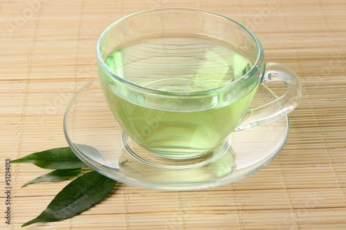 Transparent cup of green tea on bamboo mat, close up