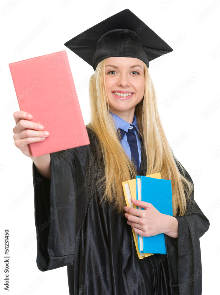 Smiling young woman in graduation gown showing book Smiling young woman in graduation gown showing book