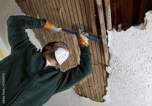 a man pulling down plaster ceiling lathe with a crowbar