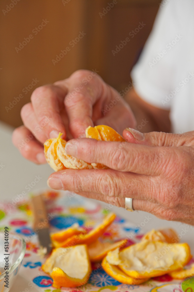Closeup of hands of senior man peeling fresh orange.