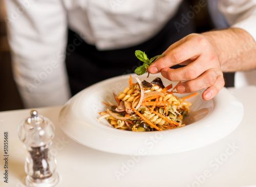 Chef decorating pasta salad with herbal leaves