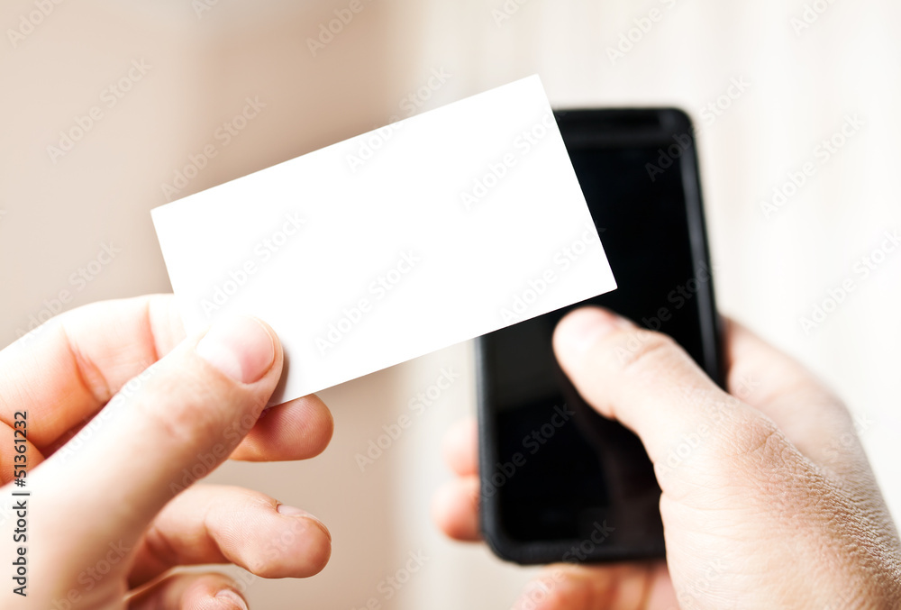 Man holding blank business card and dialing numbers on mobile ph Man holding blank business card and dialing numbers on mobile ph