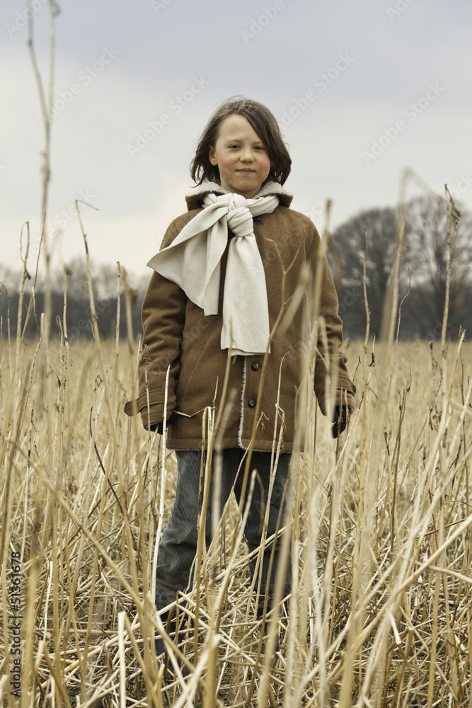 Playful funny young boy with long hair outdoor in wheat field.