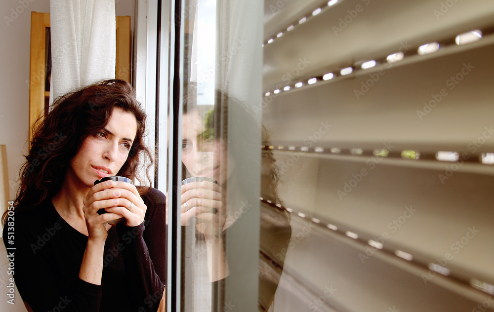 Photo of a beautiful young female drinking coffee and looking ou