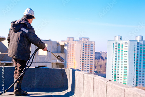 Roofer installing roofing felt by means of gas blowpipe torch