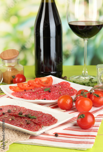 Tasty salami on plates on wooden table on natural background