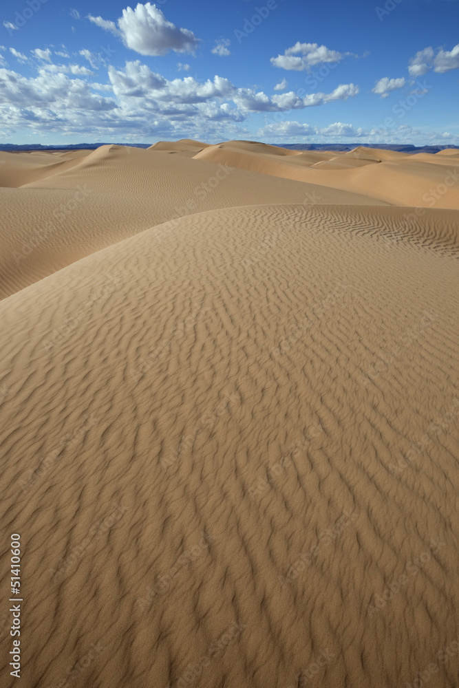 Sahara desert sand dunes with cloudy blue sky.