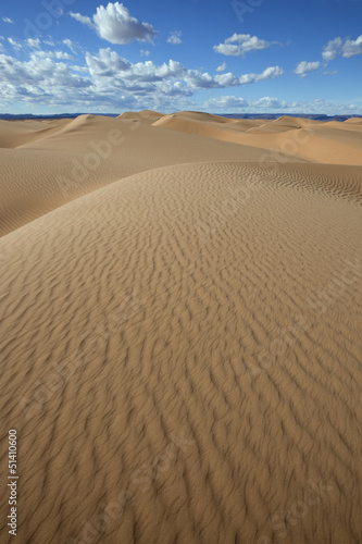 Sahara desert sand dunes with cloudy blue sky.