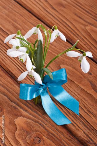 Bouquet of snowdrops tied a blue ribbon on a wooden table
