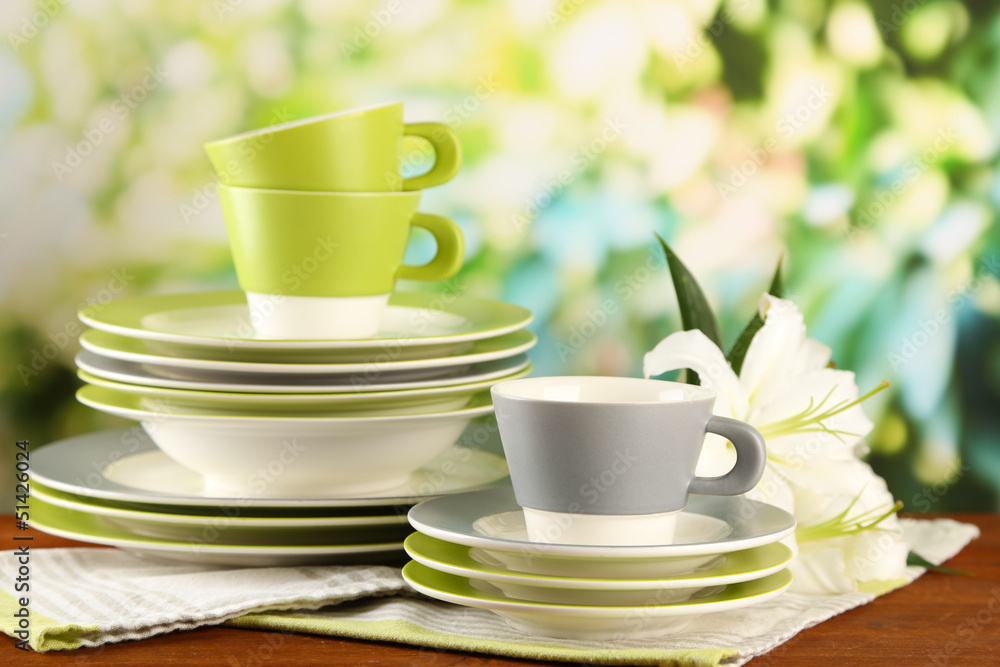 Empty plates and cups on wooden table on green background Empty plates and cups on wooden table on green background