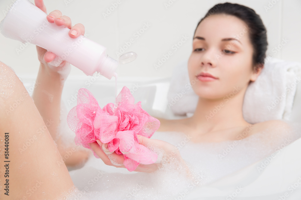 young woman in a bath with foam sponge in hand young woman in a bath with foam sponge in hand
