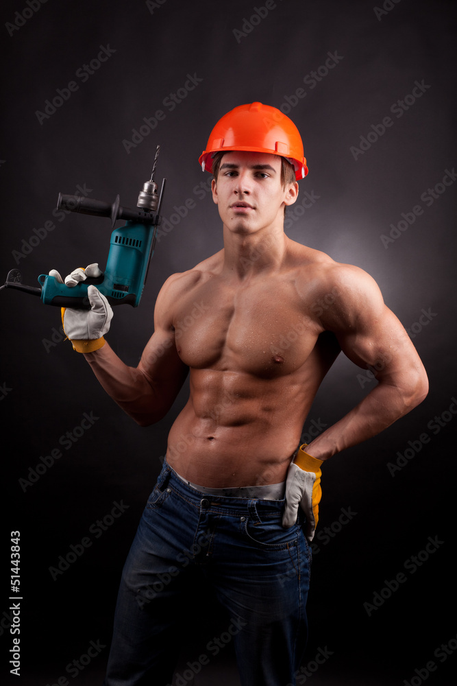 Muscular worker with an electric drill on a black background. Muscular worker with an electric drill on a black background.