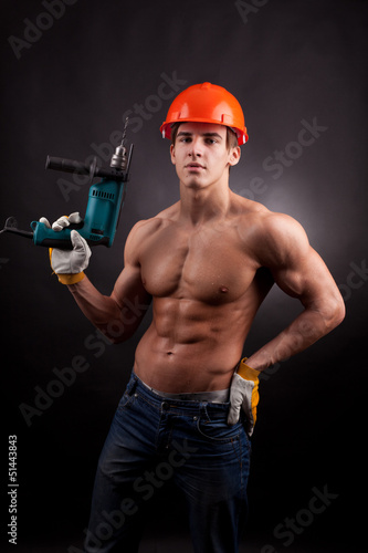 Muscular worker with an electric drill on a black background.