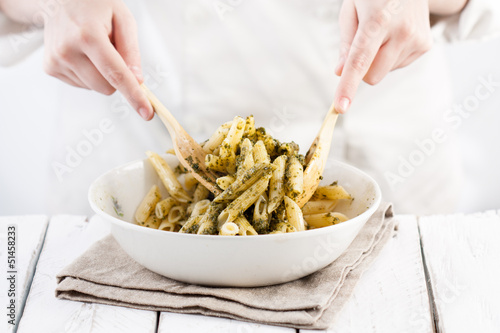 Cook mixing pesto with penne rigate pasta