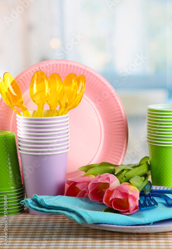 Fototapeta Naklejka Na Ścianę i Meble -  Multicolored plastic tableware on table with tulips close up