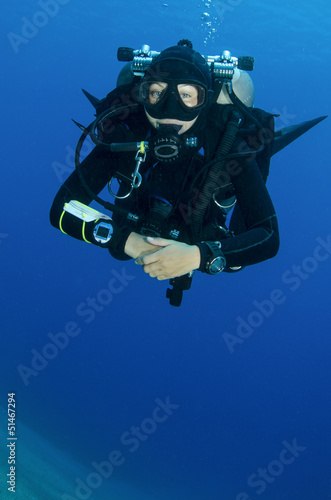 girl scuba dives in clear blue water with twin tanks