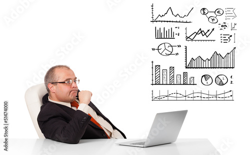 businessman sitting at desk with graphs and laptop photo