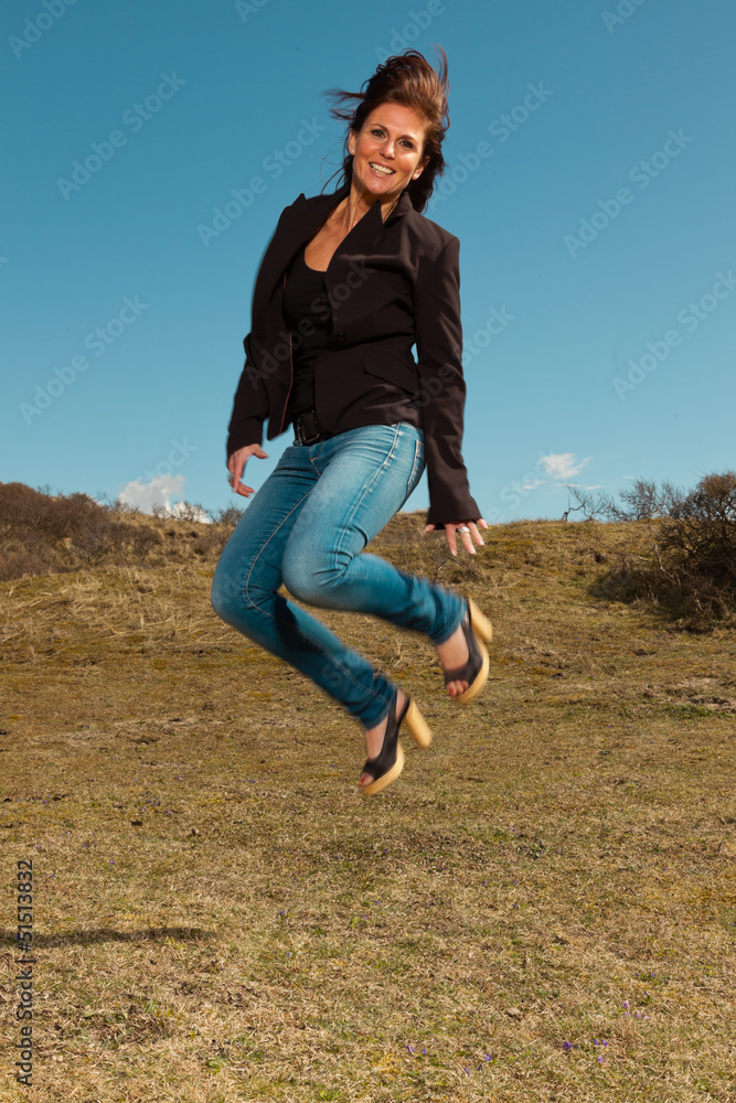 Jumping pretty brunette woman wearing brown jacket. Meadow with Jumping pretty brunette woman wearing brown jacket. Meadow with